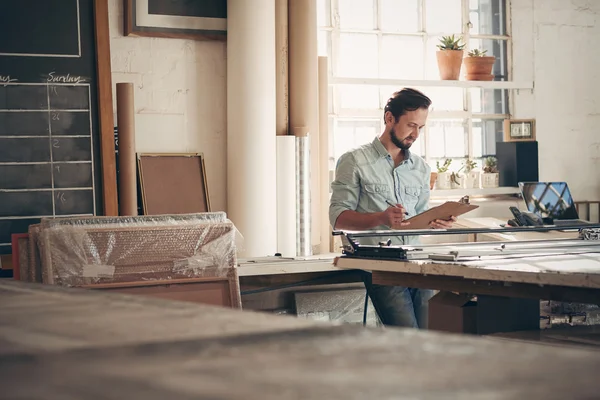 Entrepreneur in workshop checking figures on clipboard — Stock Photo, Image