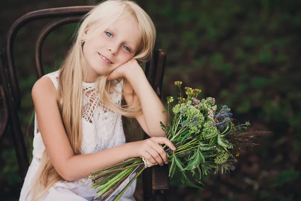 Portrét dětské holčičky na židličce s lesklou kyticí květin — Stock fotografie