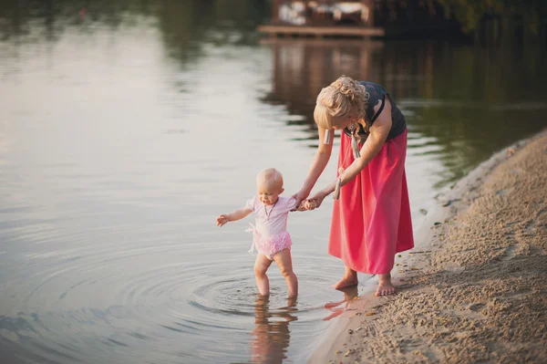 Moeder speelt met de kleine dochter in de buurt van water — Stockfoto