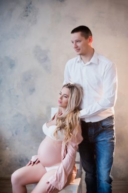 Kocası onun hamile eşi hafif bir arka plan üzerinde beyaz iç çamaşırı sarılma