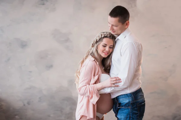 Férje átölelve terhes feleségét, a világos háttér fehér fehérnemű — Stock Fotó