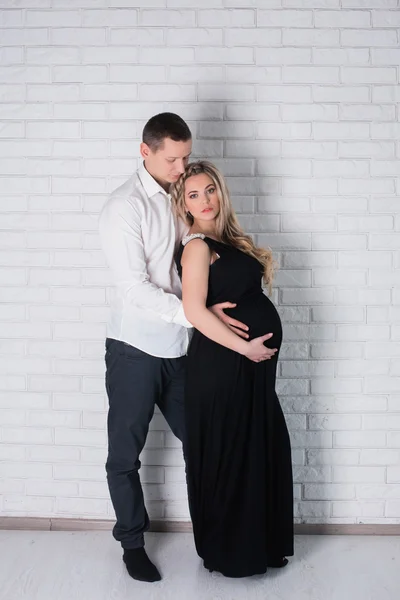 Esposo abrazando a su esposa embarazada en lencería blanca sobre un fondo claro — Foto de Stock