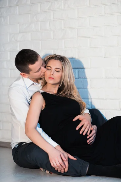 Чоловік обіймає свою вагітну дружину в білій білизні на світлому фоні — стокове фото