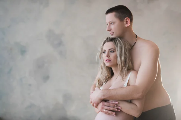 Mari étreignant sa femme enceinte en lingerie blanche sur un fond clair — Photo
