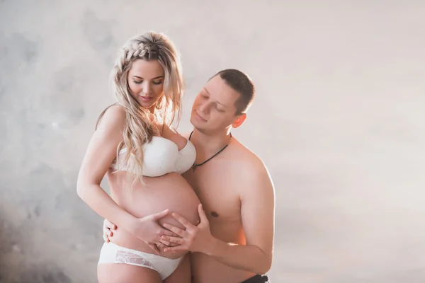 Mari étreignant sa femme enceinte en lingerie blanche sur un fond clair — Photo