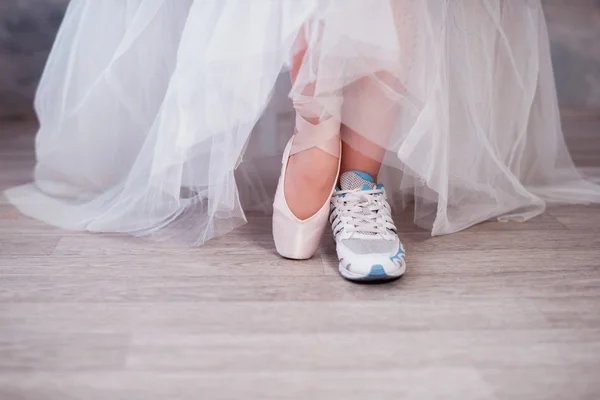 Legs of a ballerina, one foot shod in sneakers other in pointe shoes