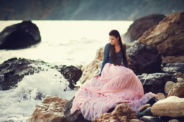 Una chica se sienta en una roca en la playa contra el cielo y el mar —  Fotos de Stock