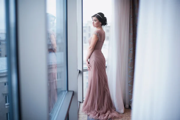 La femme dans une belle robe rose debout près de la fenêtre — Photo