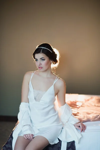 Menina bonita sentada em uma cama em uma camisa branca — Fotografia de Stock