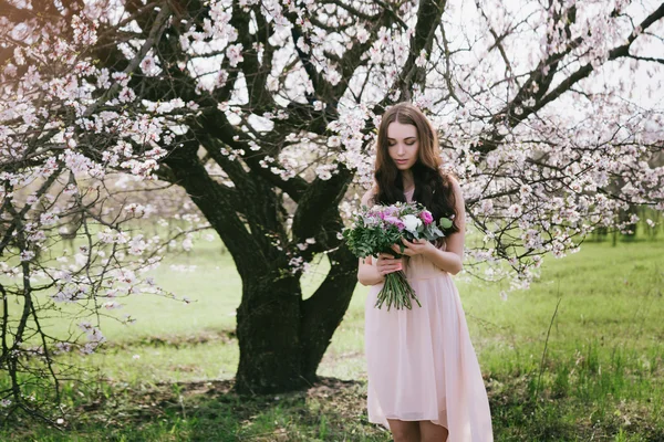 Žena v kvetoucí stromy. Žena s svatební kytice v ruce. — Stock fotografie