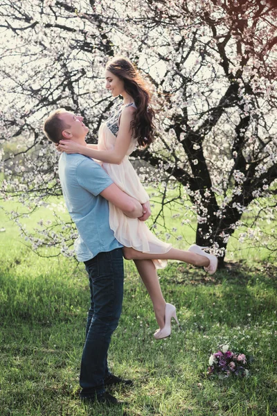 Um homem segurando uma mulher feliz em seus braços em flor jardim de primavera — Fotografia de Stock