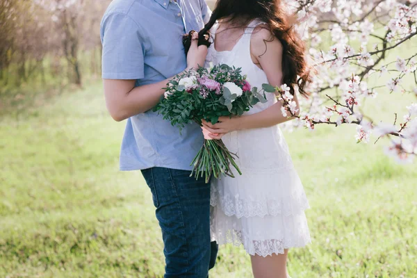 Руки молодые мужчины и женщины обнимают красивую девушку в цветущем саду — стоковое фото