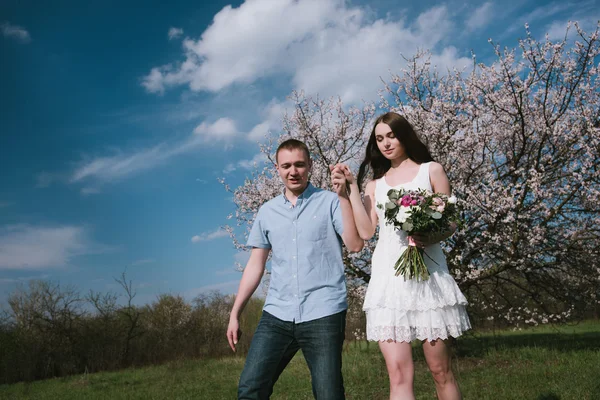 Happy couple running in bloom garden holding hand in hand on blue sky background — Stock Photo, Image