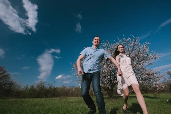 Joyeux couple courant dans le jardin fleuri tenant la main dans la main sur fond de ciel bleu — Photo