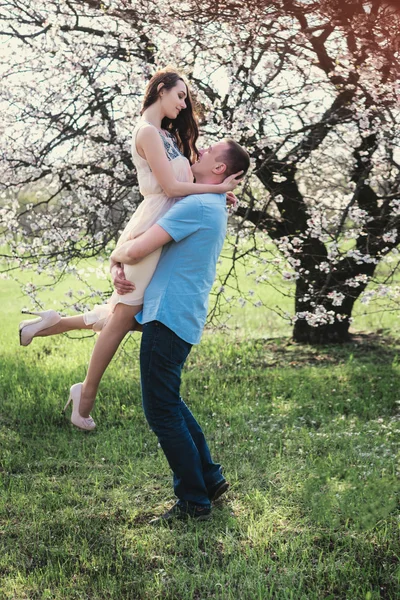 A man holding a happy woman in her arms in blossom spring garden — Stock Photo, Image