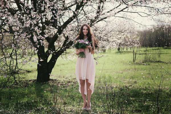 Woman in blooming trees. Woman with wedding bouquet in hands. Beautiful posing in a blooming apple garden.Spring mood. Young woman outdoors