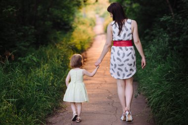 Anne kızının elini tutar ve gün batımı ışık doğada yürüyüş yürür