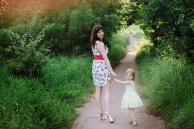 Anne kızının elini tutar ve gün batımı ışık doğada yürüyüş yürür