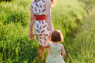 Anne kızının elini tutar ve gün batımı ışık doğada yürüyüş yürür