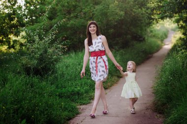 Anne kızının elini tutar ve gün batımı ışık doğada yürüyüş yürür