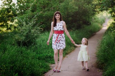 Anne kızının elini tutar ve gün batımı ışık doğada yürüyüş yürür