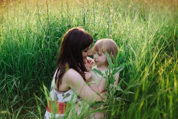 Mom kisses and hugs daughter on nature in sunsetlight