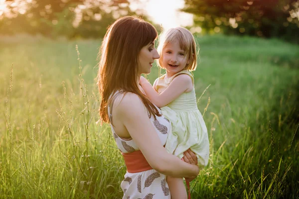 Mamá besos y abrazos hija en la naturaleza en la luz del sol —  Fotos de Stock