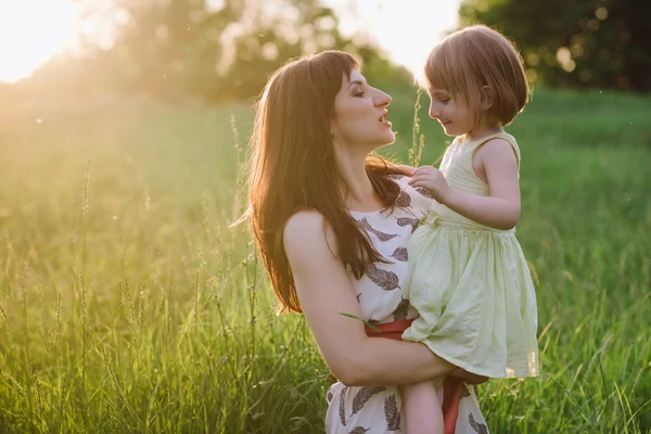 Mamá besos y abrazos hija en la naturaleza en la luz del sol —  Fotos de Stock