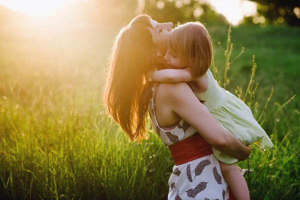 Moeder kusjes en knuffels van dochter op natuur in sunsetlight — Stockfoto