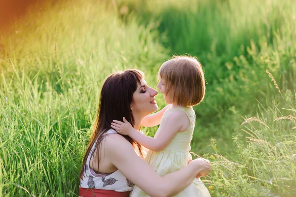 Mamá besos y abrazos hija en la naturaleza en la luz del sol —  Fotos de Stock