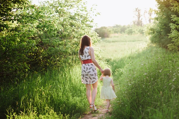 Mamá mantiene la mano de su hija y camina por la naturaleza bajo la luz del atardecer —  Fotos de Stock