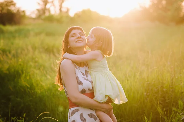 Mamá besos y abrazos hija en la naturaleza en la luz del sol —  Fotos de Stock