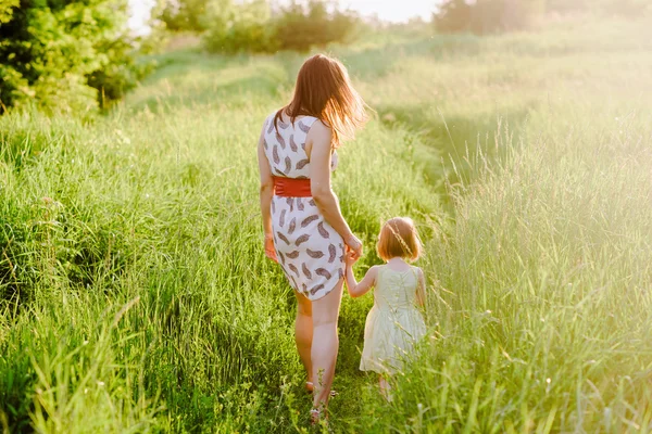 Mamá mantiene la mano de su hija y camina por la naturaleza bajo la luz del atardecer —  Fotos de Stock