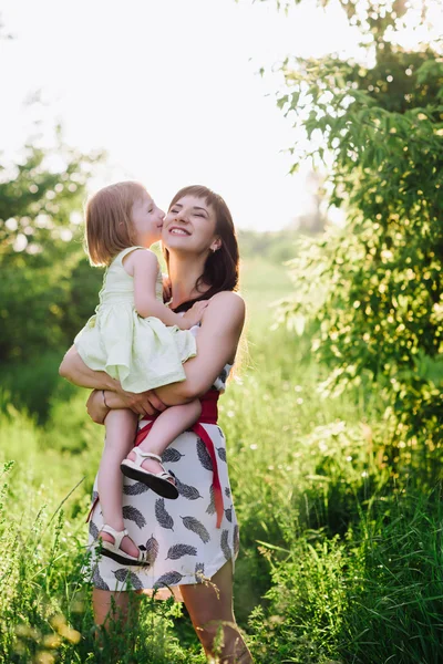 Mãe beijos e abraços filha na natureza ao pôr do sol — Fotografia de Stock