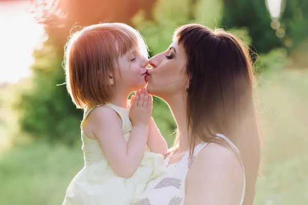 Mamá besos y abrazos hija en la naturaleza en la luz del sol —  Fotos de Stock