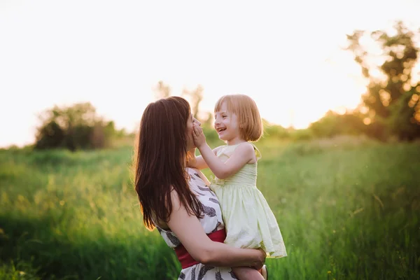 Mamá besos y abrazos hija en la naturaleza en la luz del sol —  Fotos de Stock