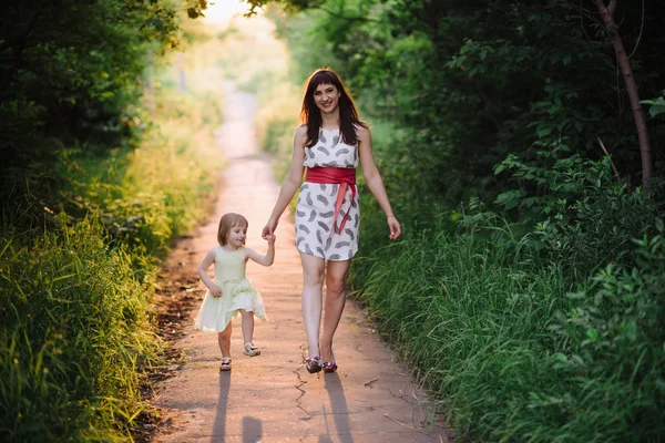 Μαμά κρατά το χέρι της κόρης του και περπατά τον περίπατο στη φύση στο φως του ηλιοβασιλέματος — Φωτογραφία Αρχείου