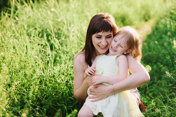 Mom kisses and hugs daughter on nature in sunsetlight