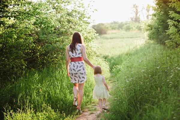 Mom keeps daughter\'s hand and walks the walk on the nature in sunset light