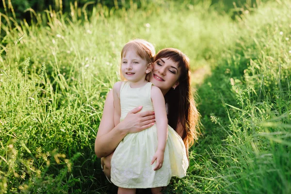 Mom kisses and hugs daughter on nature in sunsetlight