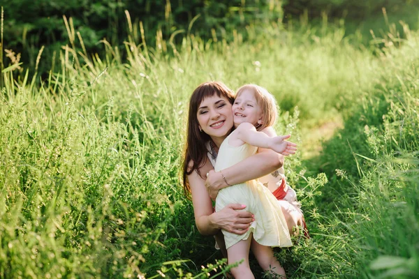 Mom kisses and hugs daughter on nature in sunsetlight