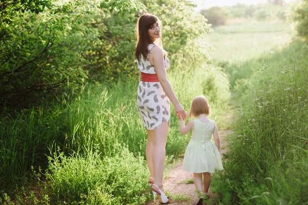 Maman garde la main de sa fille et marche sur la nature au coucher du soleil — Photo