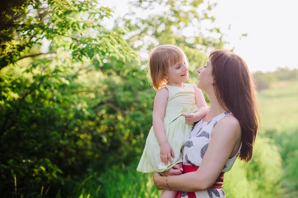 Mamá besos y abrazos hija en la naturaleza en la luz del sol —  Fotos de Stock