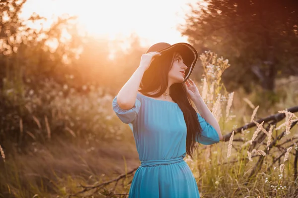 Retrato de una hermosa chica en un sombrero en un campo a la luz del atardecer —  Fotos de Stock