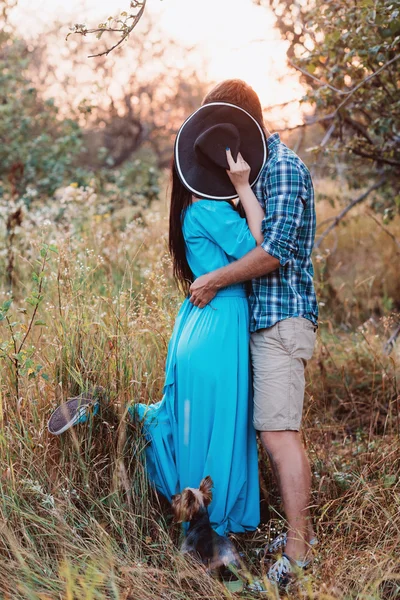 The guy and the girl standing on nature, embrace and kiss under the guise of a wide hat — Stock Photo, Image