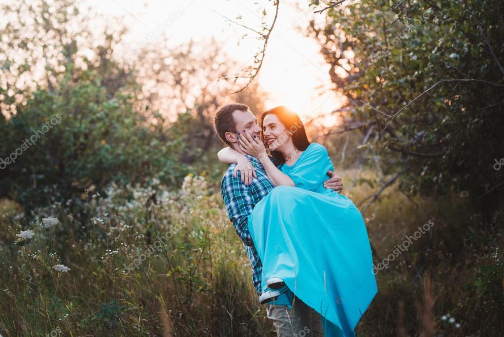 Young man carries in his arms a young attractive girl in a park