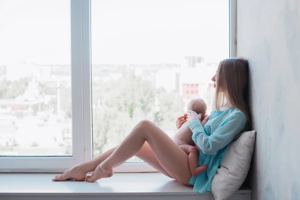 Baby in a tender embrace of yong mother at the windowstill — Stock Photo, Image