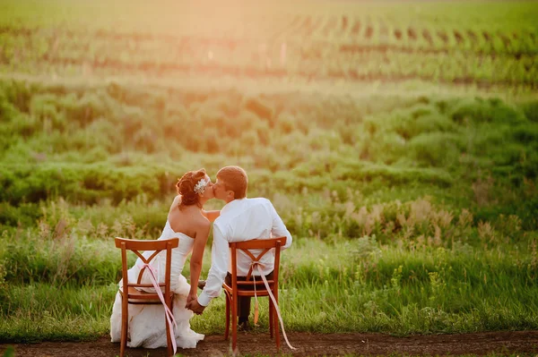 Belle jeune mariée et marié chaises assises dans la lumière du coucher du soleil — Photo