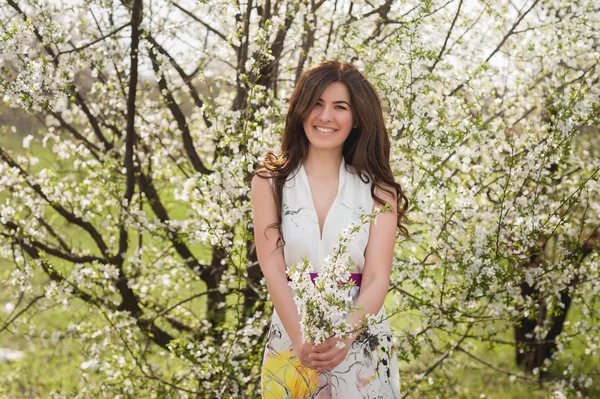 Жінка з красивим волоссям у пишному весняному саду посміхається і радіє, краса, макіяж, волосся — стокове фото