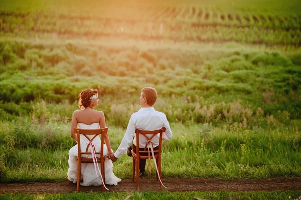 Belle jeune mariée et marié chaises assises dans la lumière du coucher du soleil — Photo